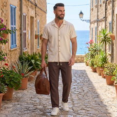 Man walking down a picturesque street with ocean view, holding a brown leather bag.