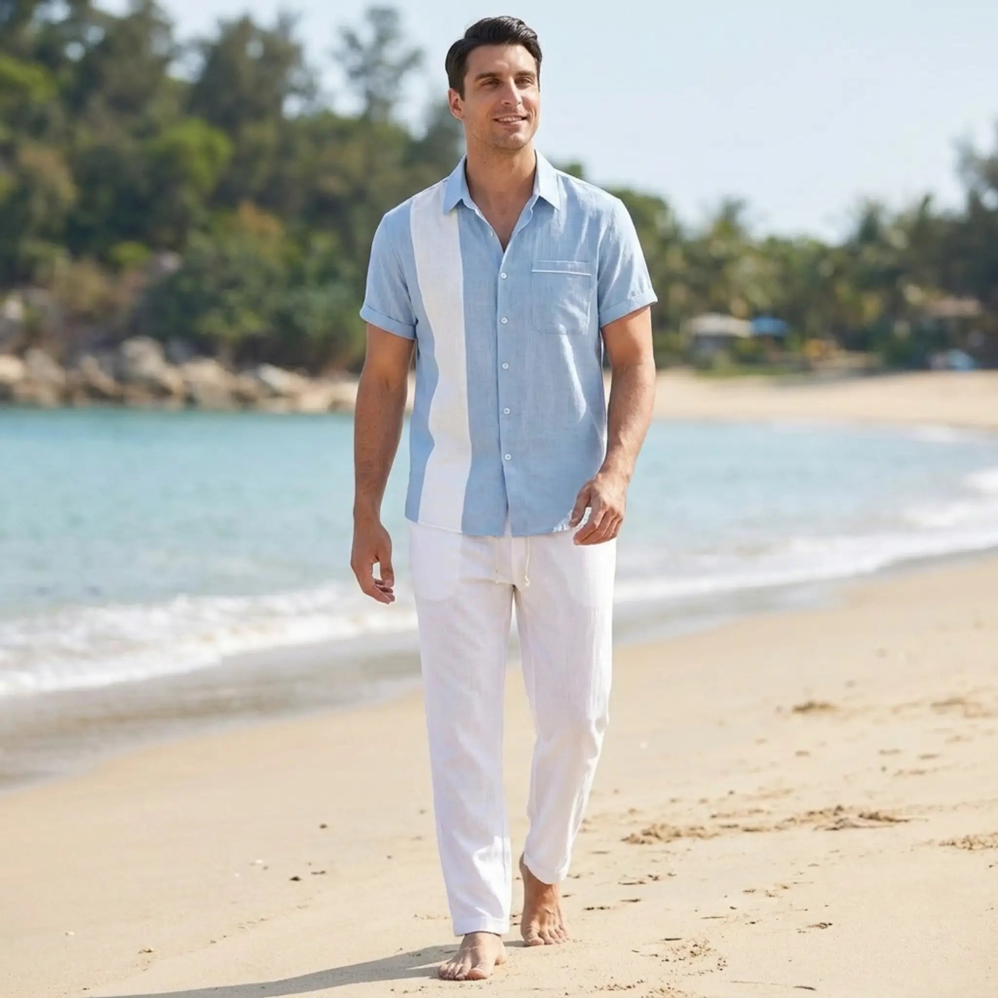 Man walking on a beach wearing a light blue shirt and white pants.
