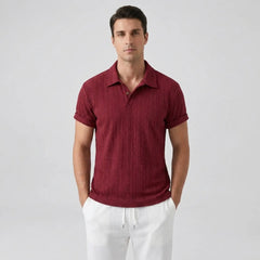 Man wearing a Maroon textured polo shirt and white pants on a light gray background