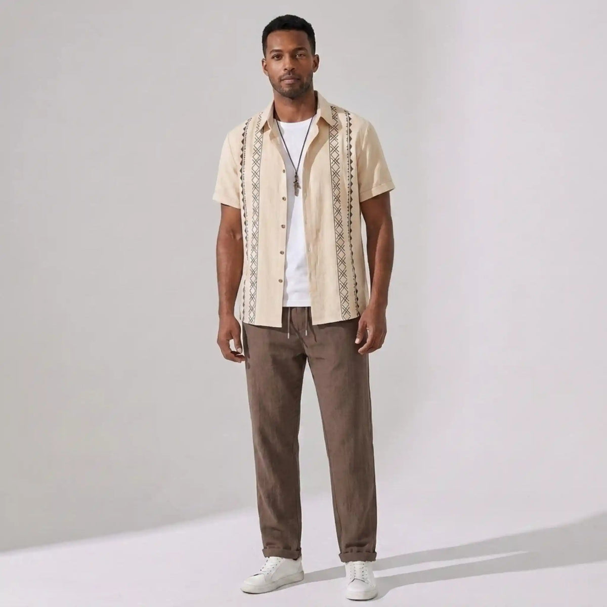 Man wearing a beige patterned shirt and pants on a gray background