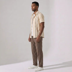 Man wearing a beige patterned shirt and pants against a plain background