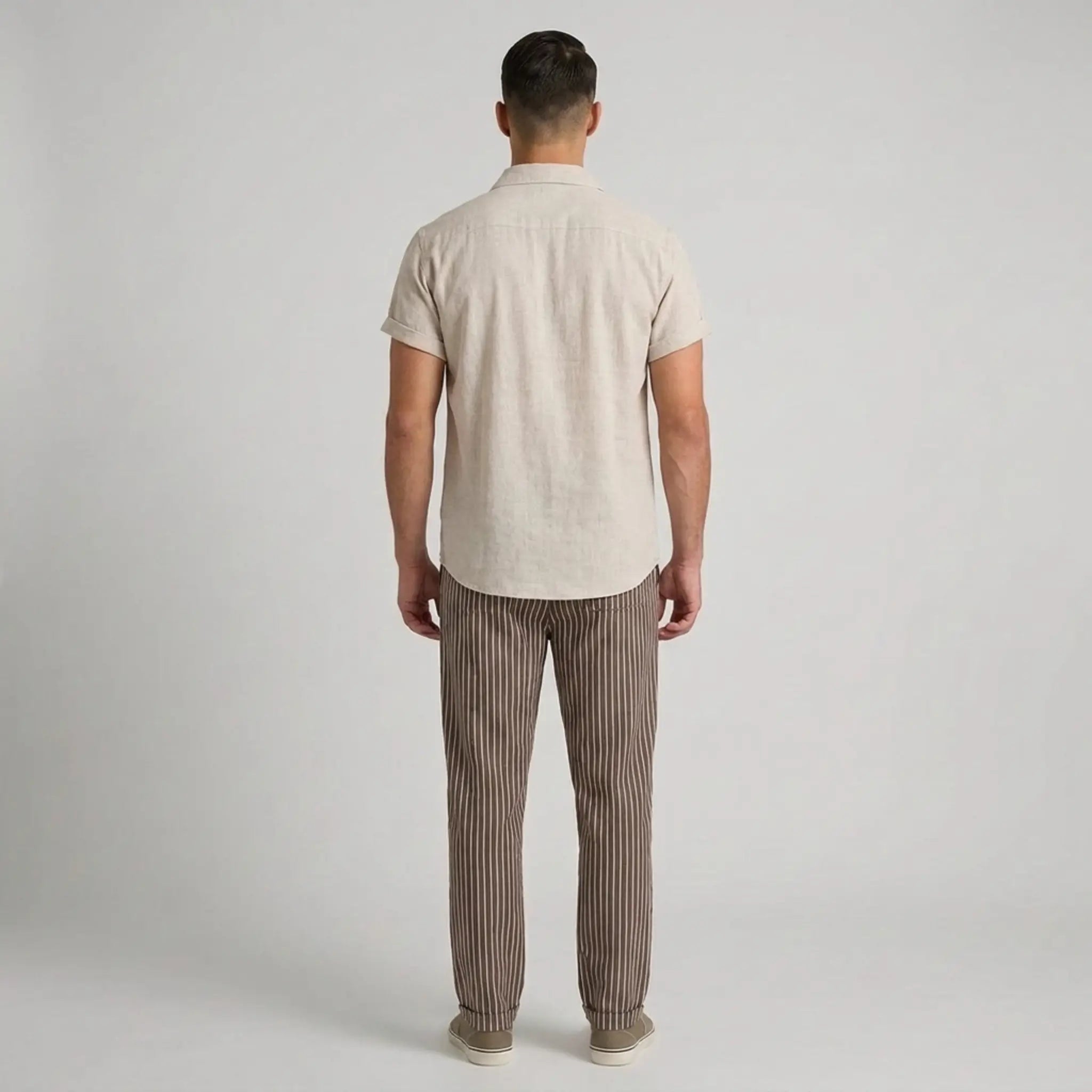 Man wearing a beige shirt and striped pants against a plain background