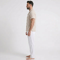 Man wearing a beige shirt and white pants on a plain background