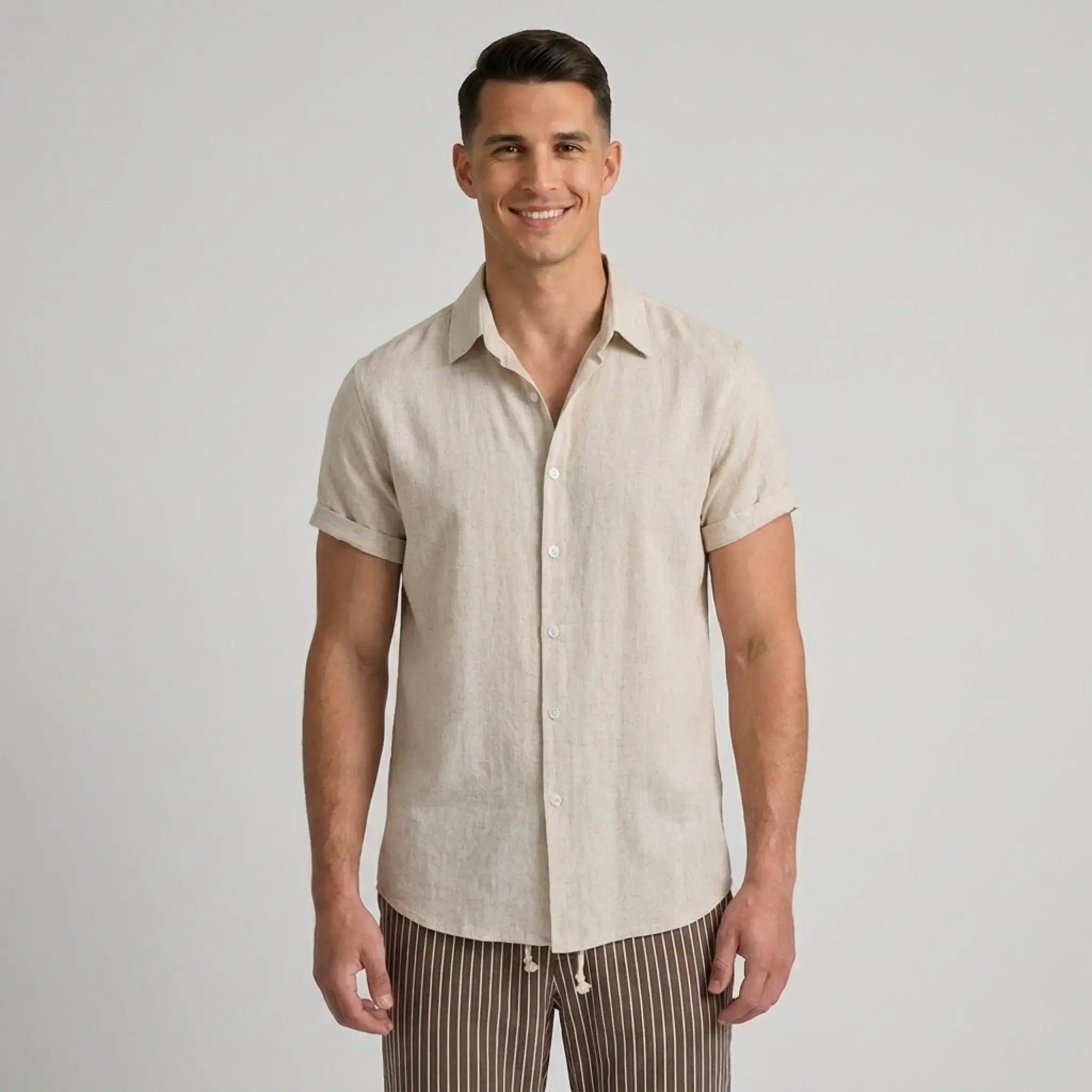 Man wearing a beige short-sleeve shirt and striped pants on a plain background