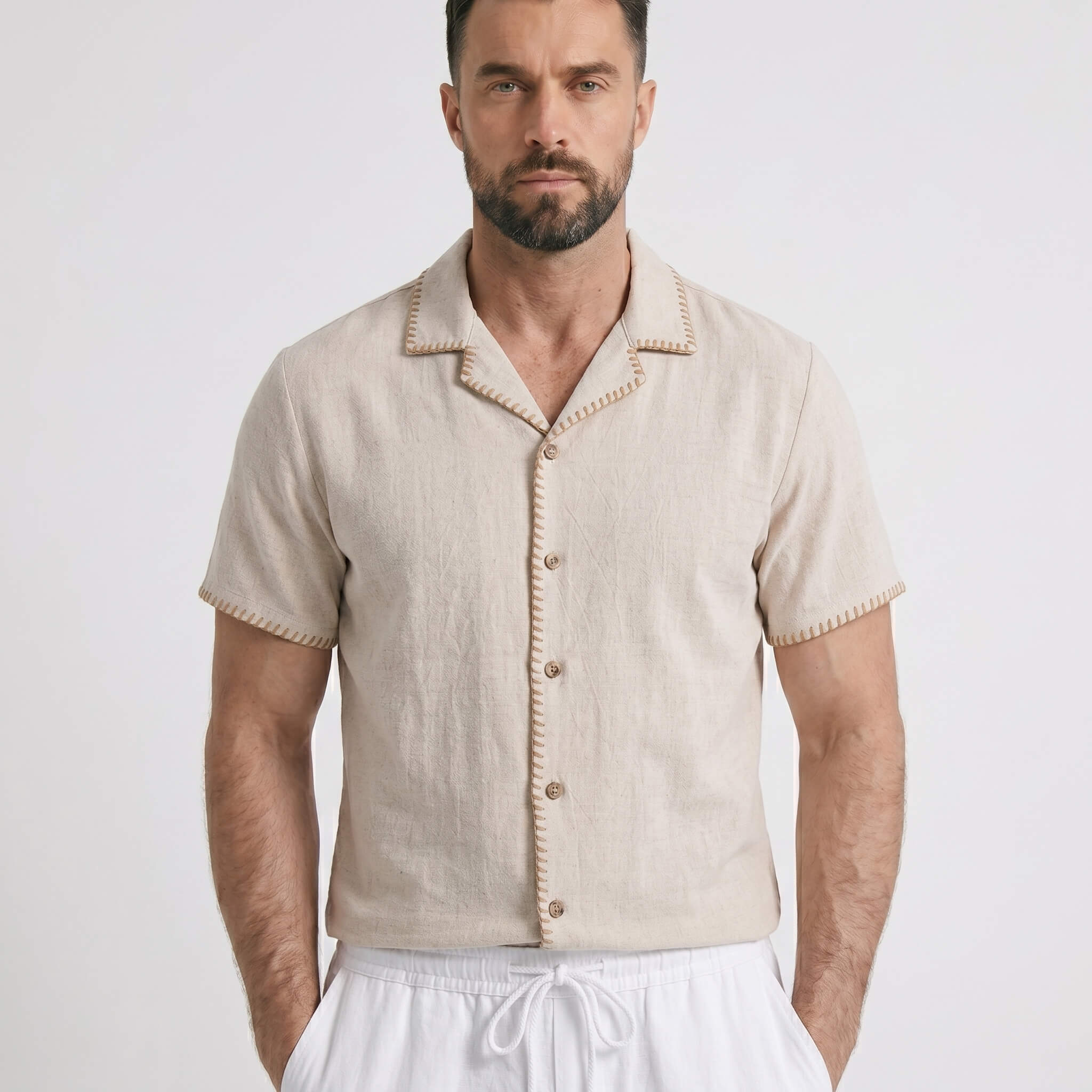 Man wearing a beige short-sleeve shirt with white pants on a light gray background