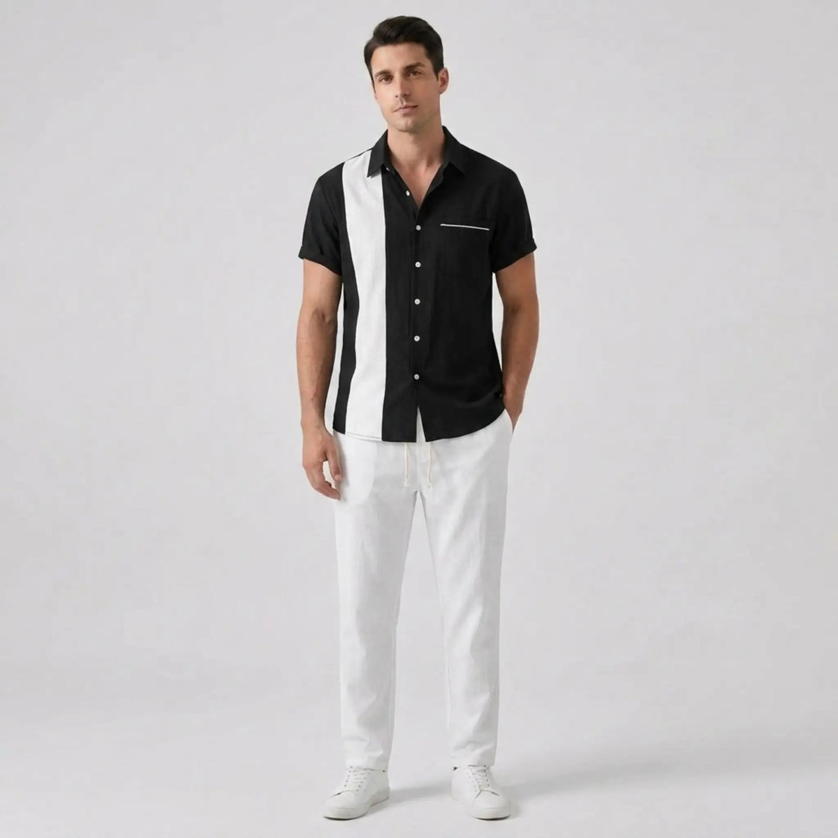 Man wearing a black and white shirt with white pants on a light gray background