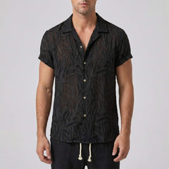 Man wearing a black patterned shirt against a plain background