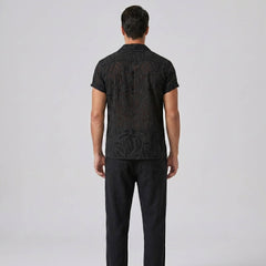 Man wearing a black patterned shirt and pants on a gray background