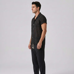 Man wearing a black patterned shirt and pants on a light gray background