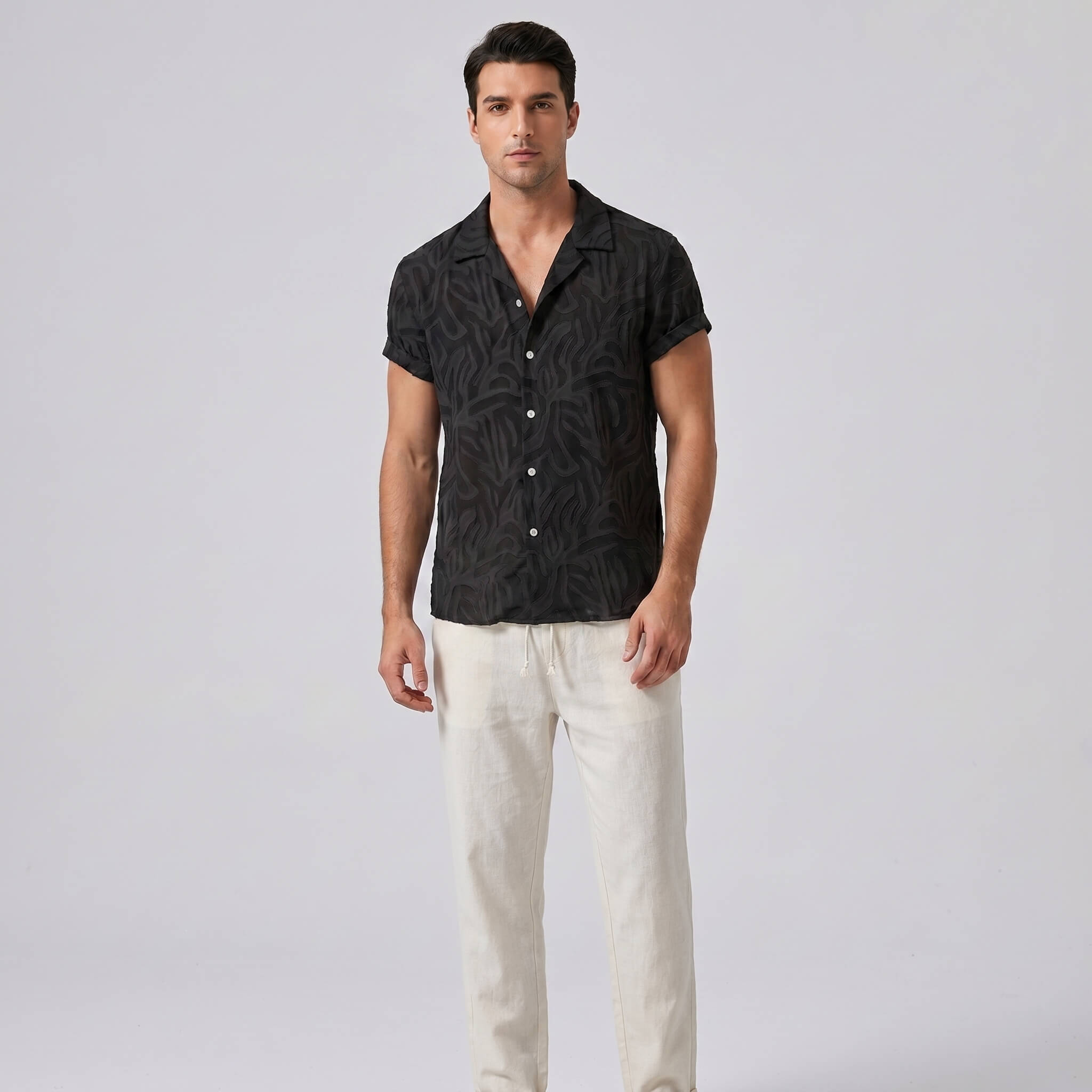 Man wearing a black patterned shirt and white pants on a light gray background
