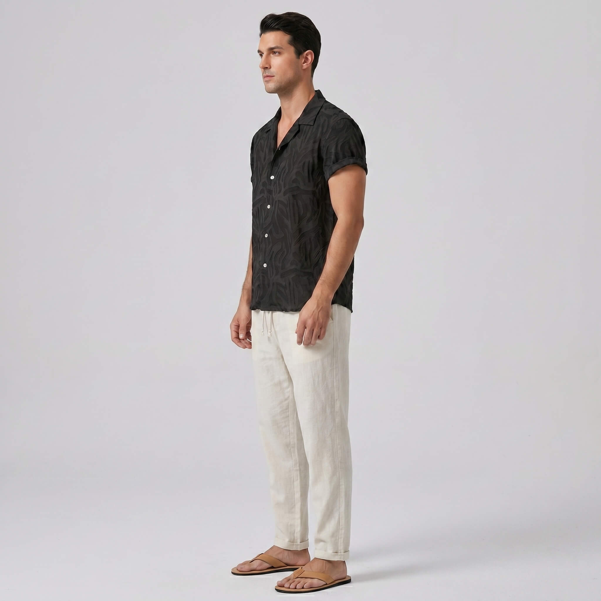 Man wearing a black patterned shirt and white pants on a plain background