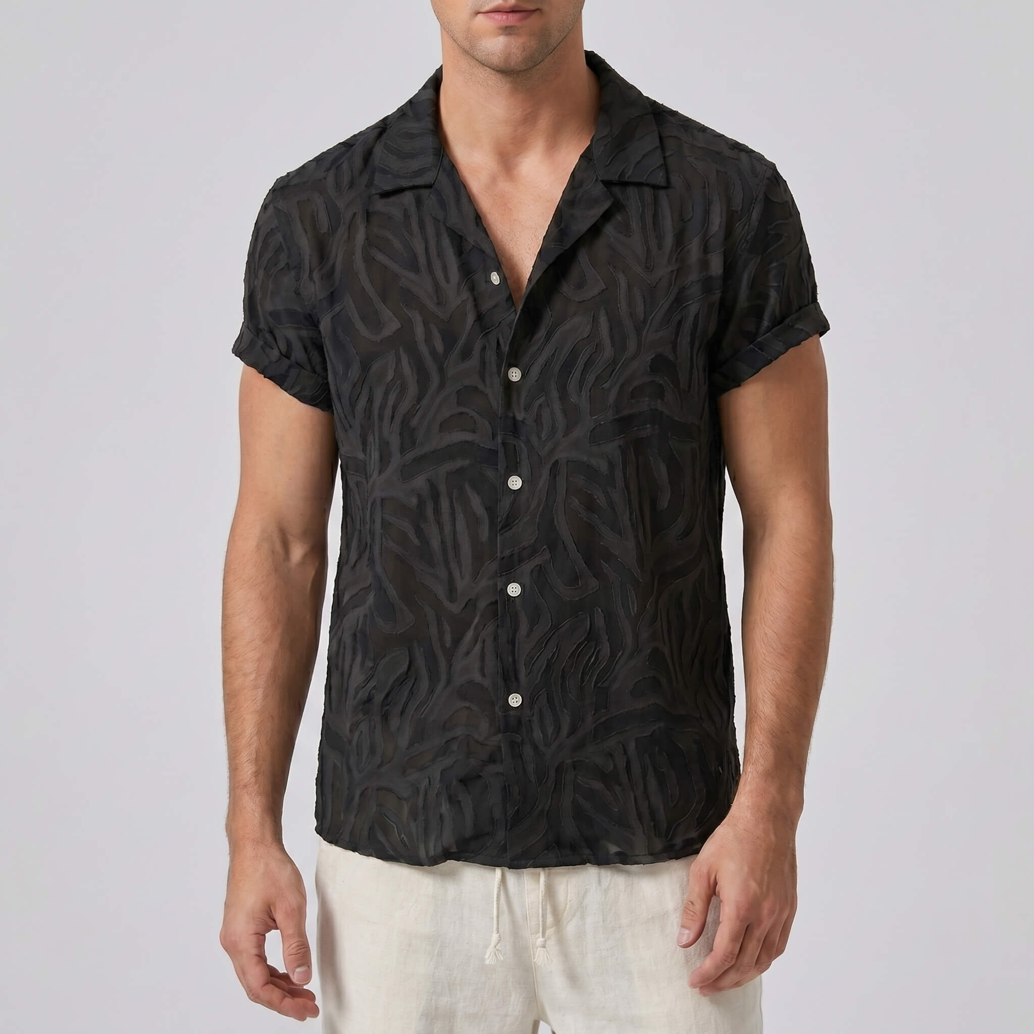 Man wearing a black patterned shirt with white pants on a plain background