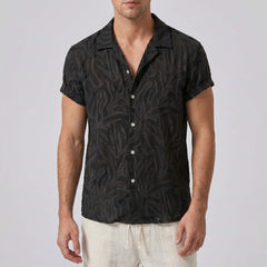 Man wearing a black patterned shirt with white pants on a plain background