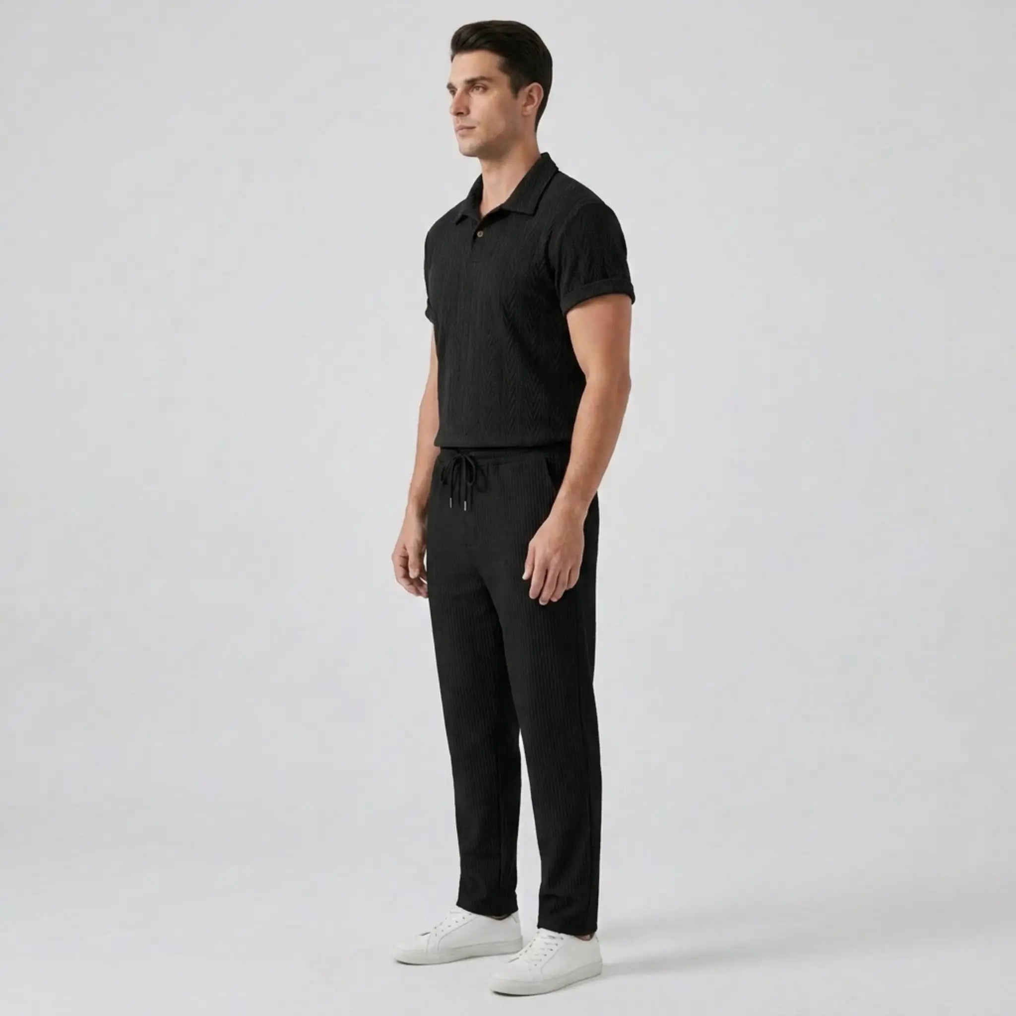 Man wearing a black polo shirt and pants with white shoes on a light gray background
