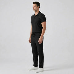 Man wearing a black polo shirt and pants with white shoes on a light gray background
