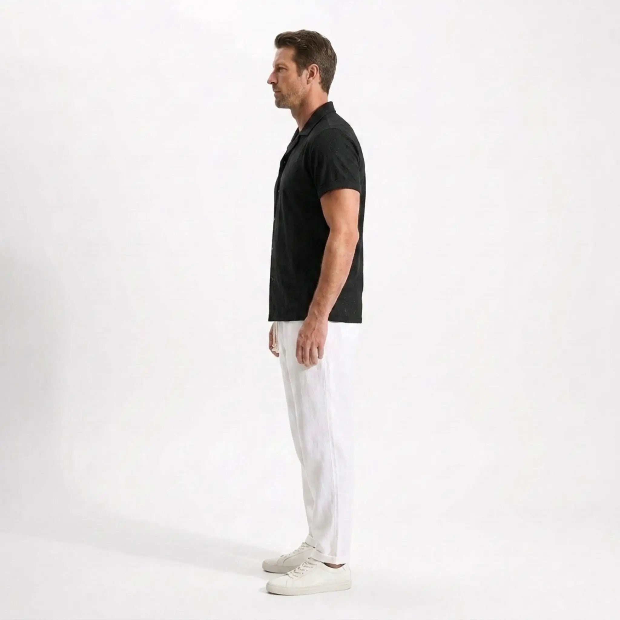 Man wearing a black polo shirt and white pants side view on a white background