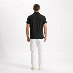 Man wearing a black polo shirt and white pants on a white background