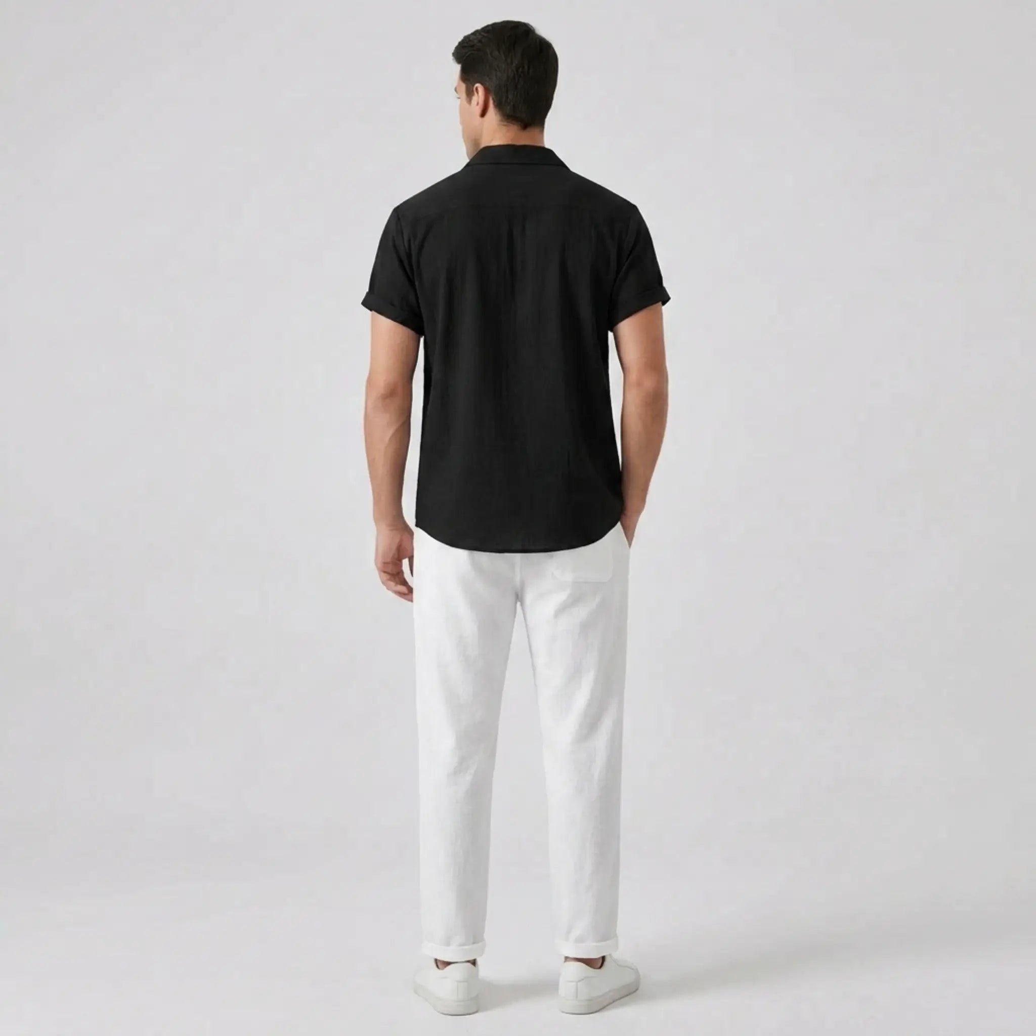 Man wearing a black shirt and white pants on a light gray background