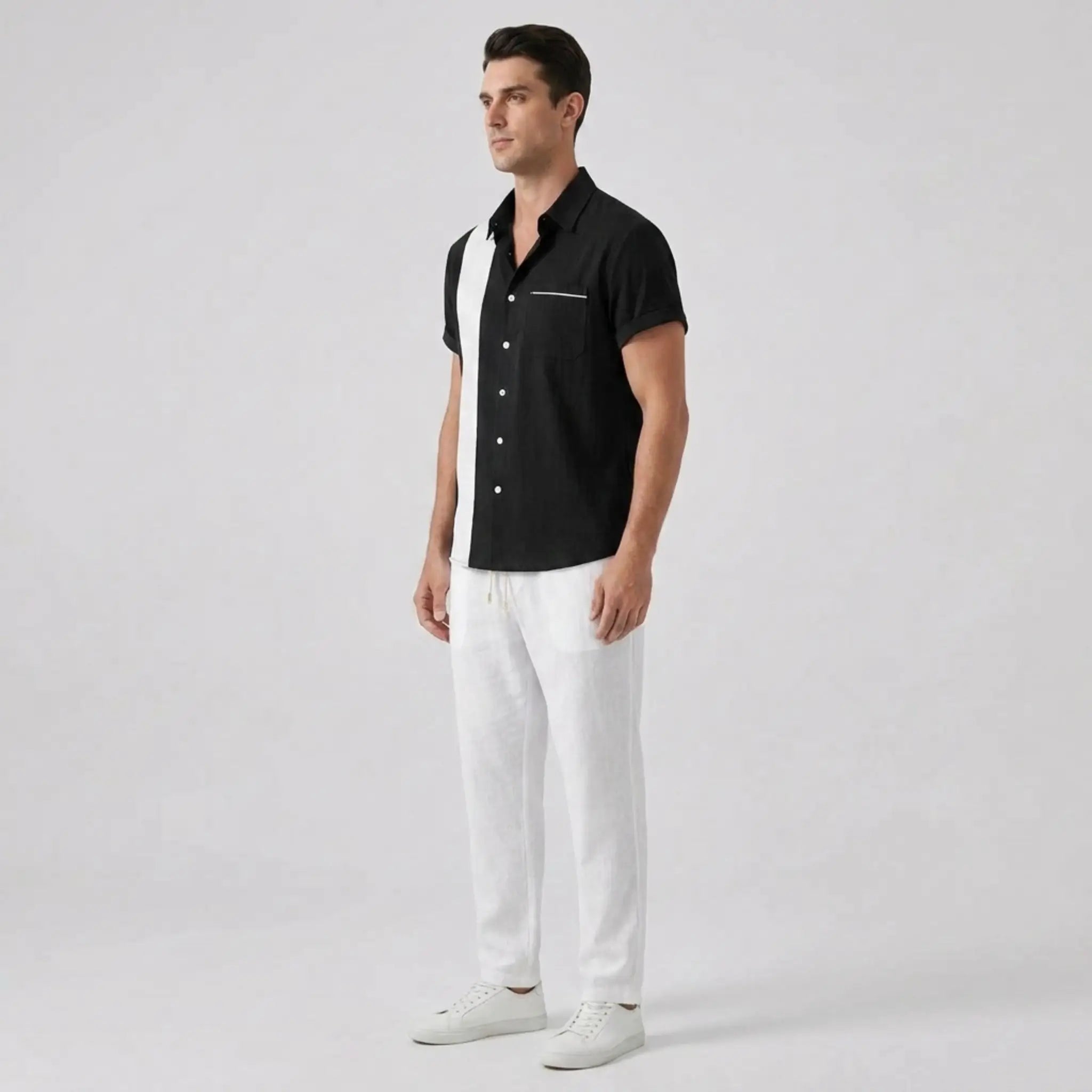 Man wearing a black short-sleeve shirt and white pants on a light gray background
