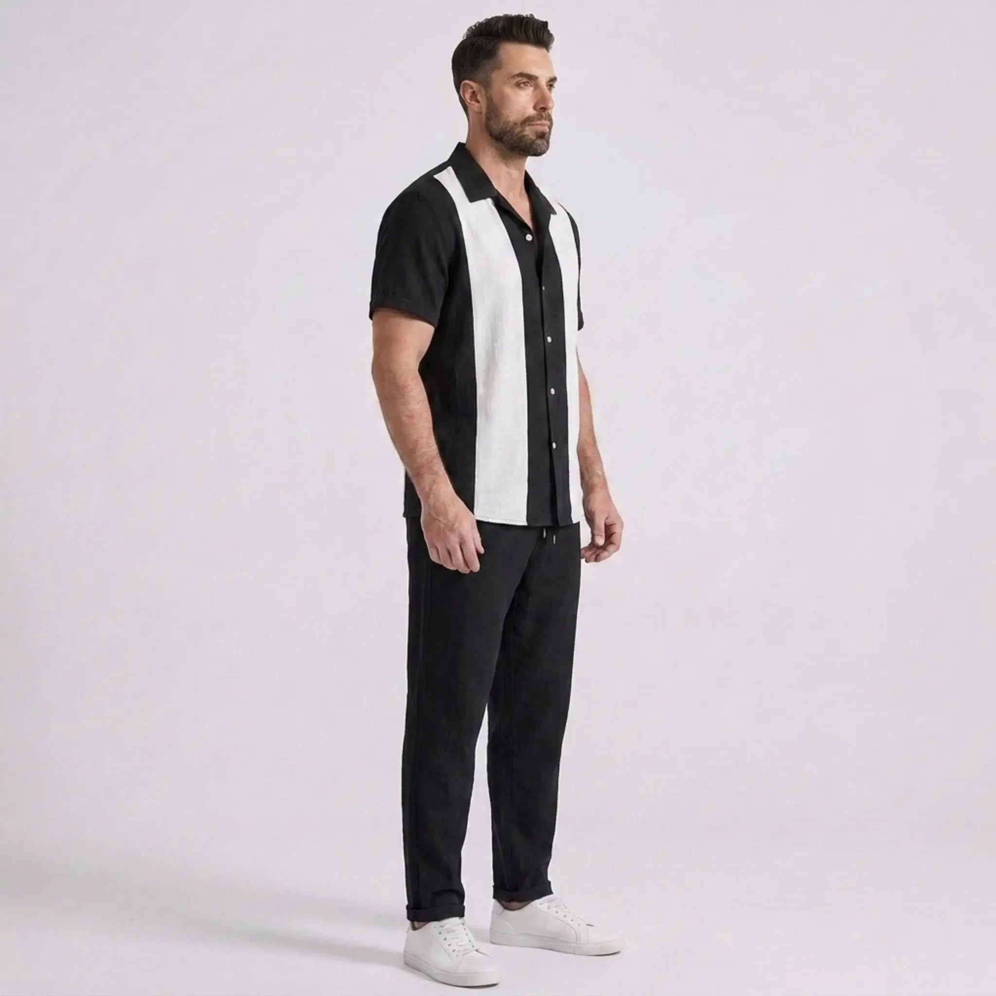 Man wearing a black and white striped shirt with black pants on a light gray background