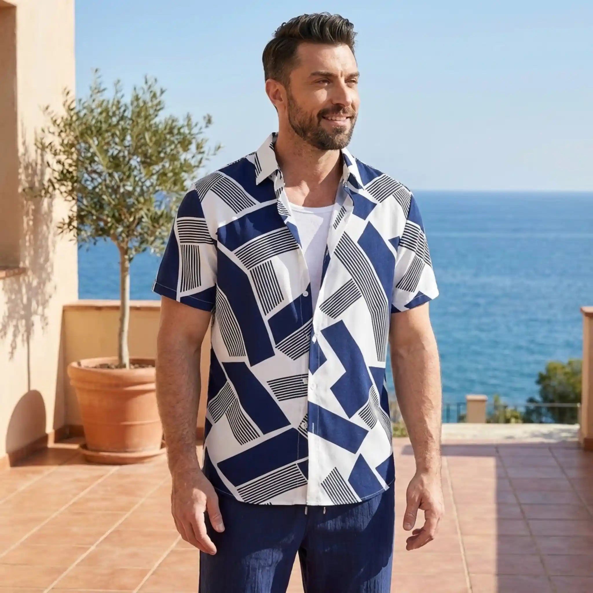 Man wearing a blue and white geometric patterned shirt standing on a patio with ocean view