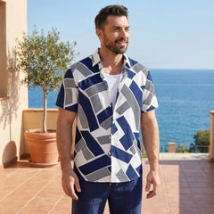 Man wearing a blue and white geometric patterned shirt standing on a patio with ocean view