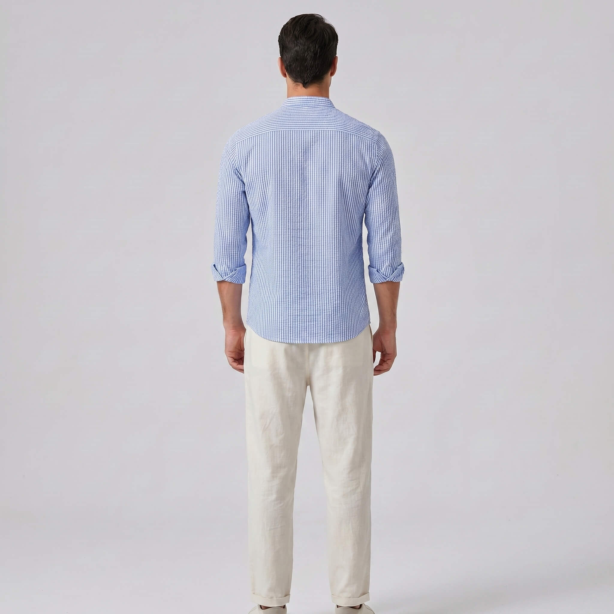 Man wearing a blue checkered shirt and white pants on a light gray background
