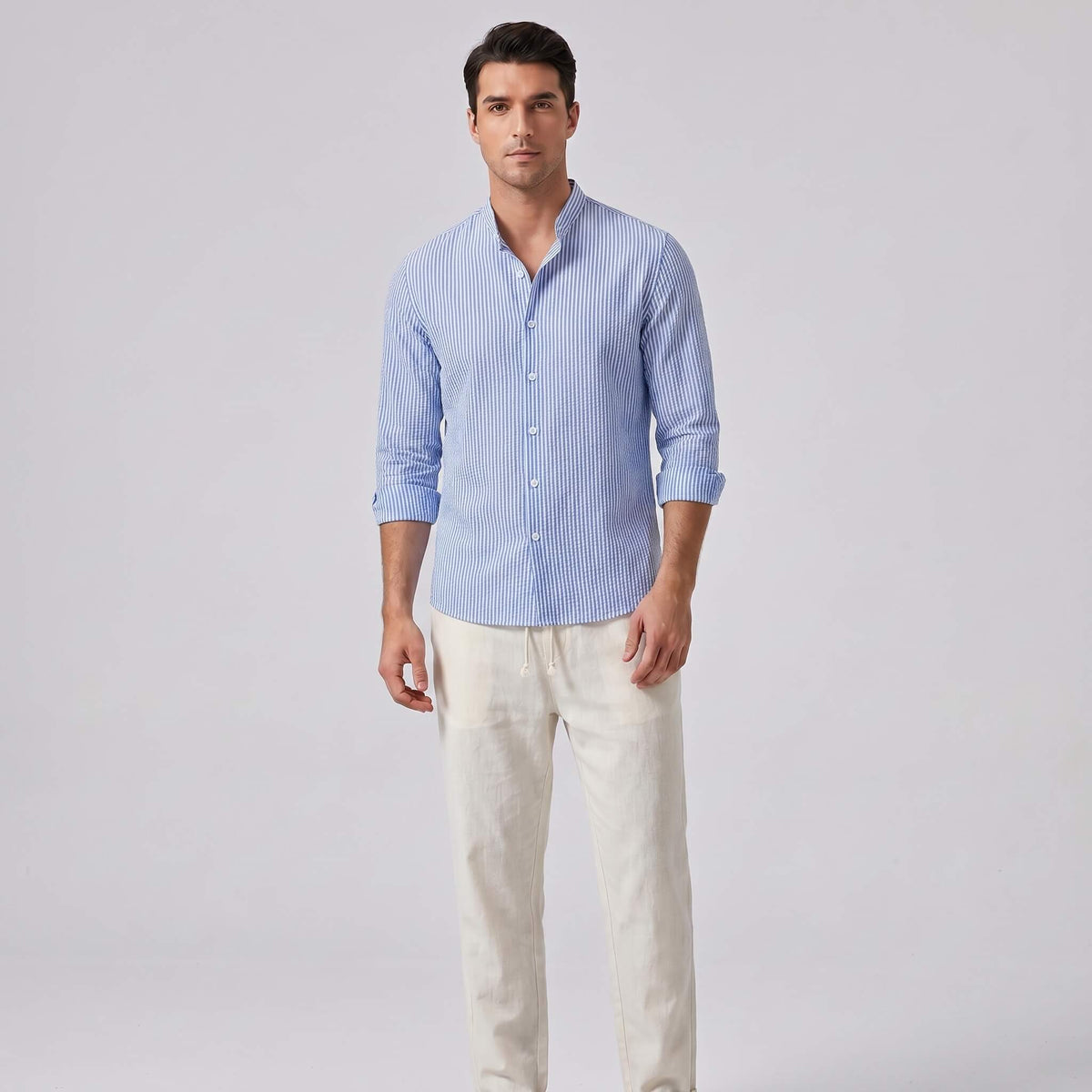 Man wearing a blue striped shirt and light-colored pants on a gray background