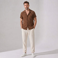 Man wearing a brown patterned shirt and beige pants against a plain background