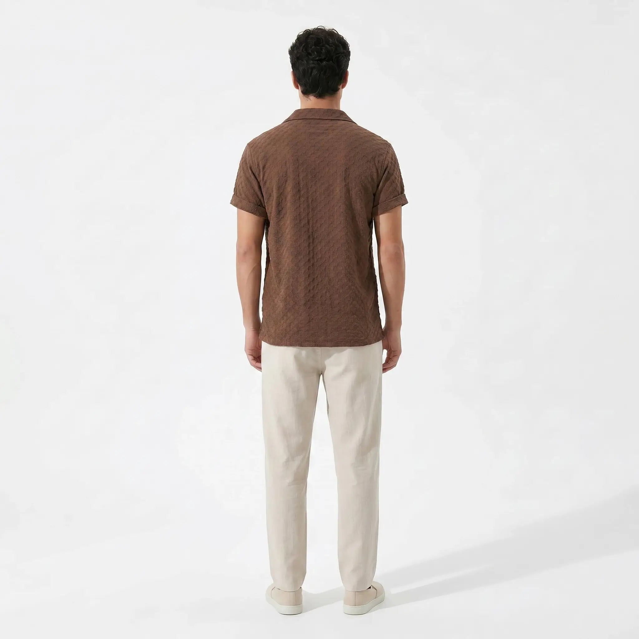 Man wearing a brown polo shirt and beige pants on a white background