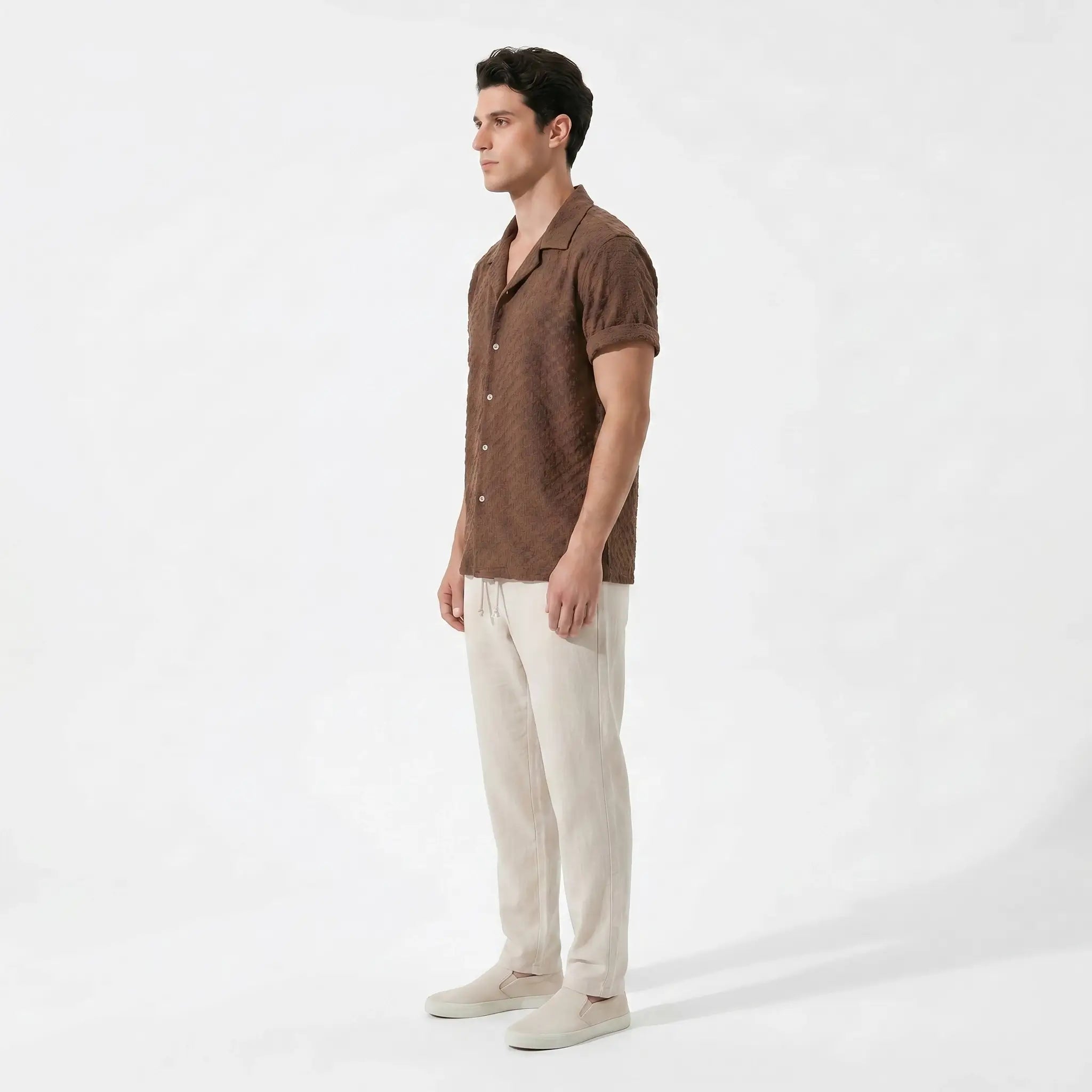 Man wearing a brown short-sleeve shirt and beige pants on a white background