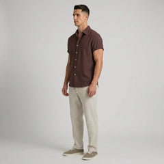 Man wearing a brown short-sleeve shirt and light-colored pants on a plain background