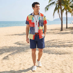 Man wearing a colorful shirt and navy shorts on a beach with palm trees and ocean in the background.