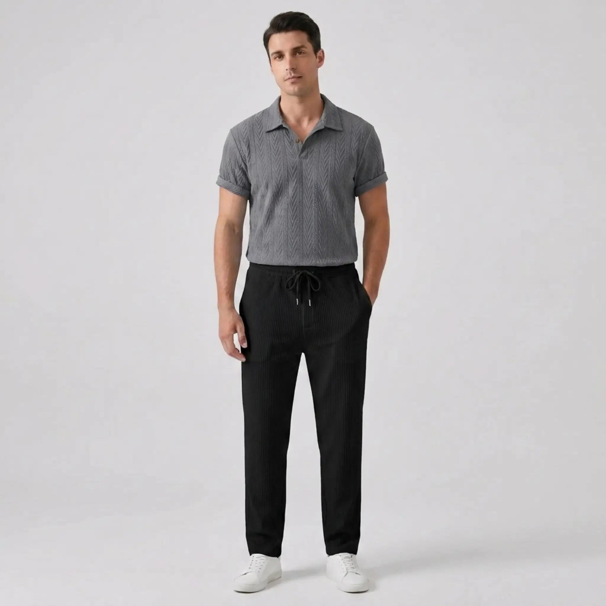 Man wearing a gray patterned polo shirt and black pants on a white background