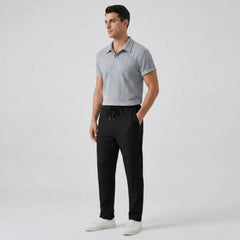 Man wearing a gray patterned short-sleeve shirt and black pants side view on a light gray background