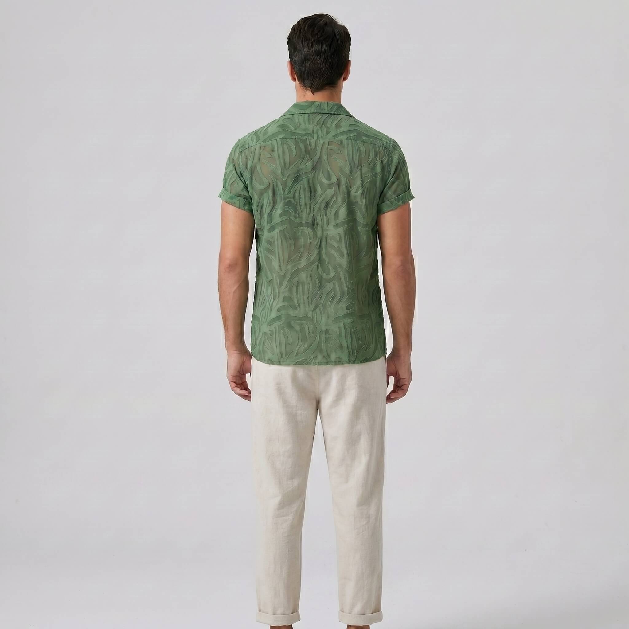 Man wearing a green patterned shirt and beige pants on a white background