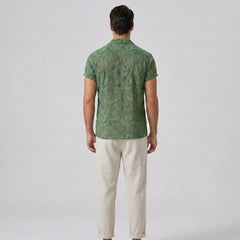 Man wearing a green patterned shirt and beige pants on a white background