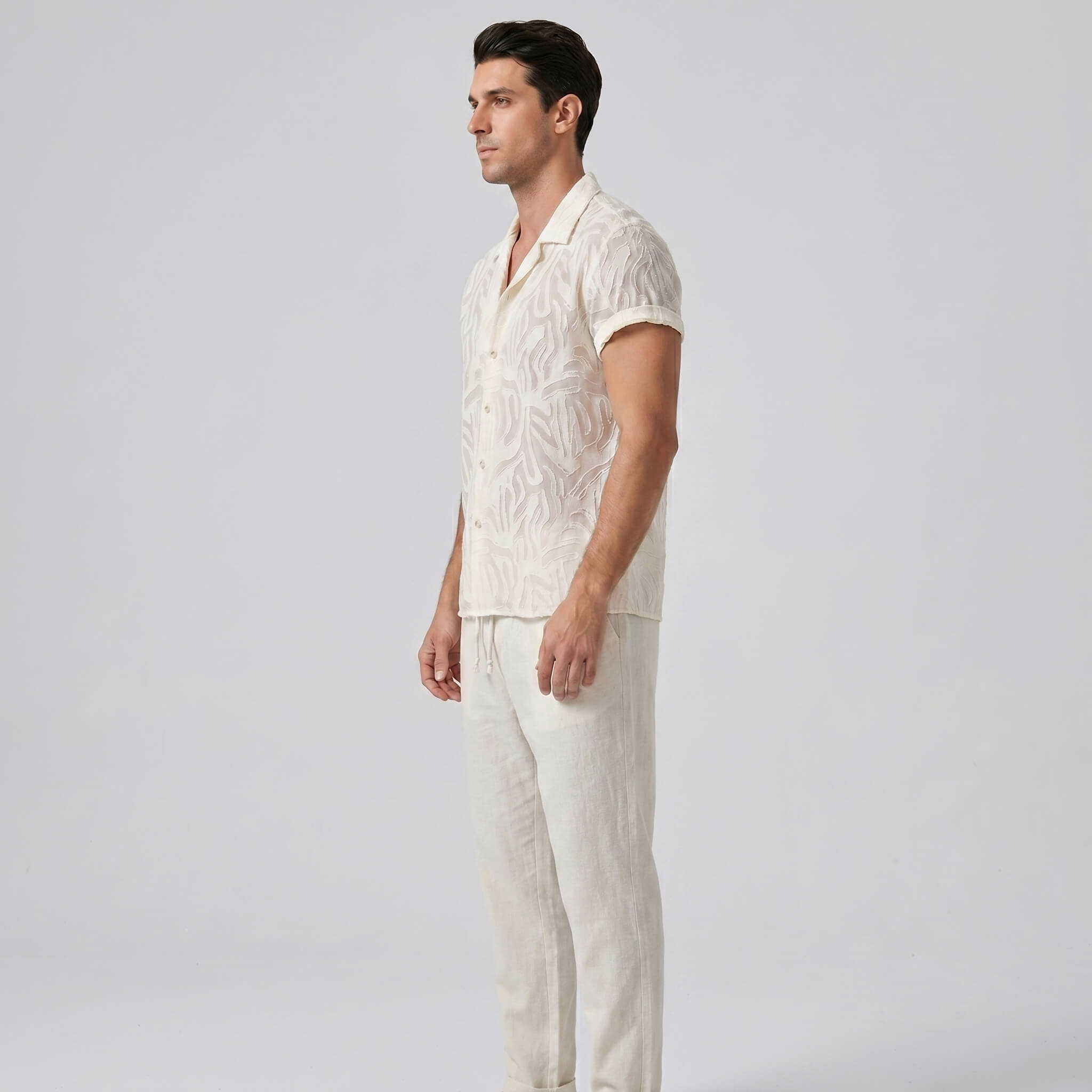 Man wearing a light-colored shirt and pants against a plain background
