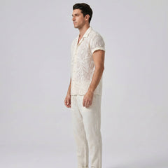 Man wearing a light-colored shirt and pants against a plain background