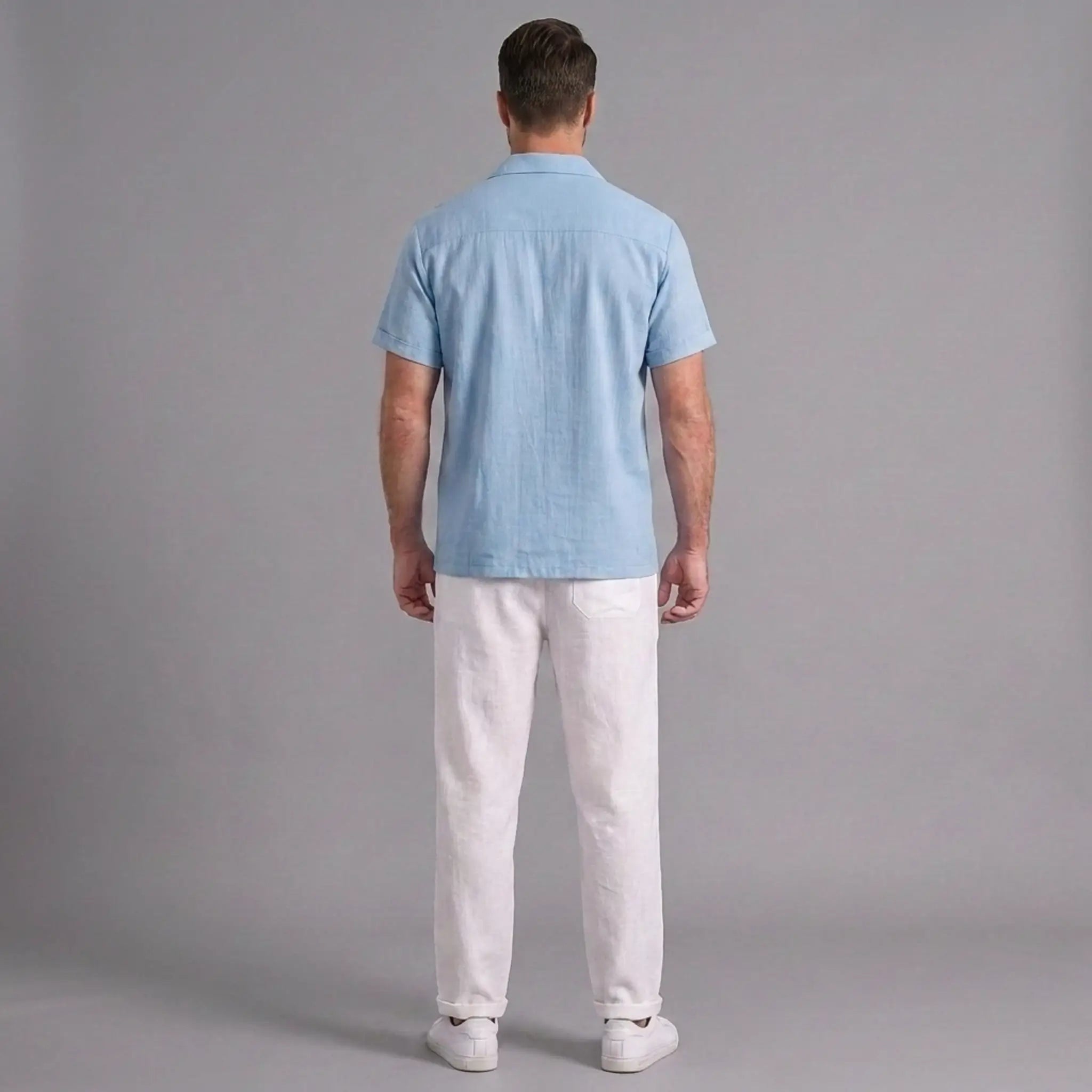 Man wearing a light blue shirt and white pants against a gray background