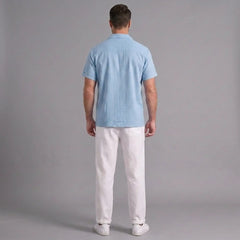 Man wearing a light blue shirt and white pants against a gray background
