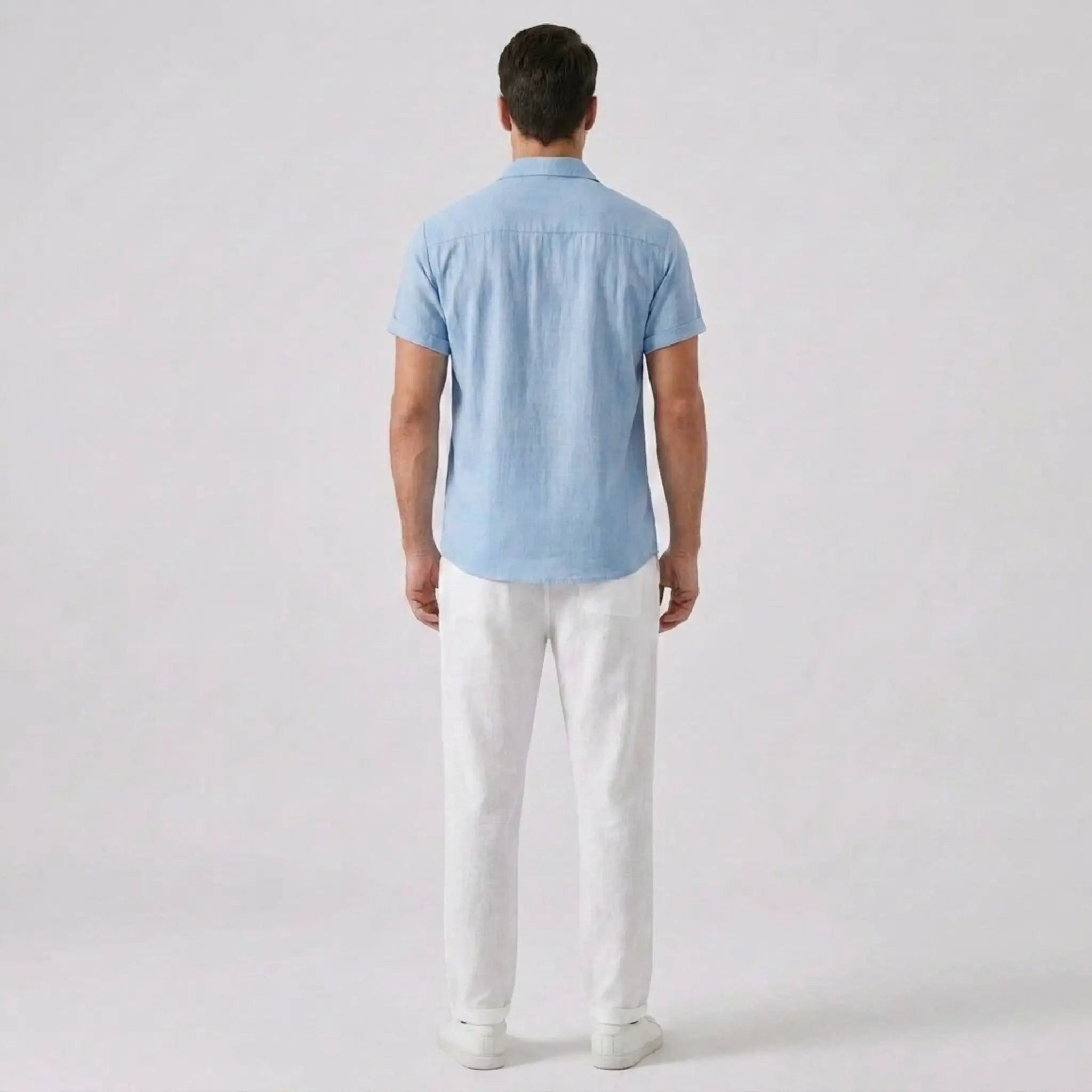 Man wearing a light blue shirt and white pants on a plain background