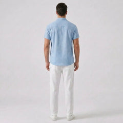 Man wearing a light blue shirt and white pants on a plain background
