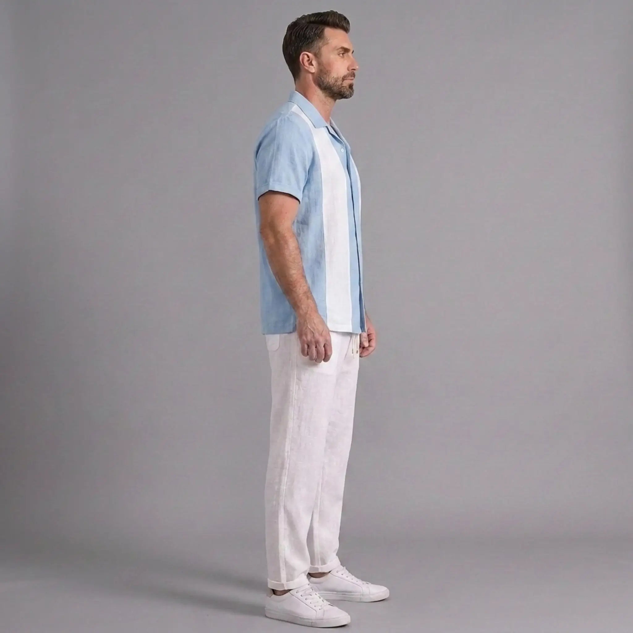 Man wearing a light blue shirt and white pants standing against a gray background
