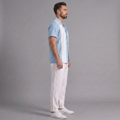 Man wearing a light blue shirt and white pants standing against a gray background