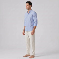 Man wearing a light blue striped shirt and white pants on a gray background