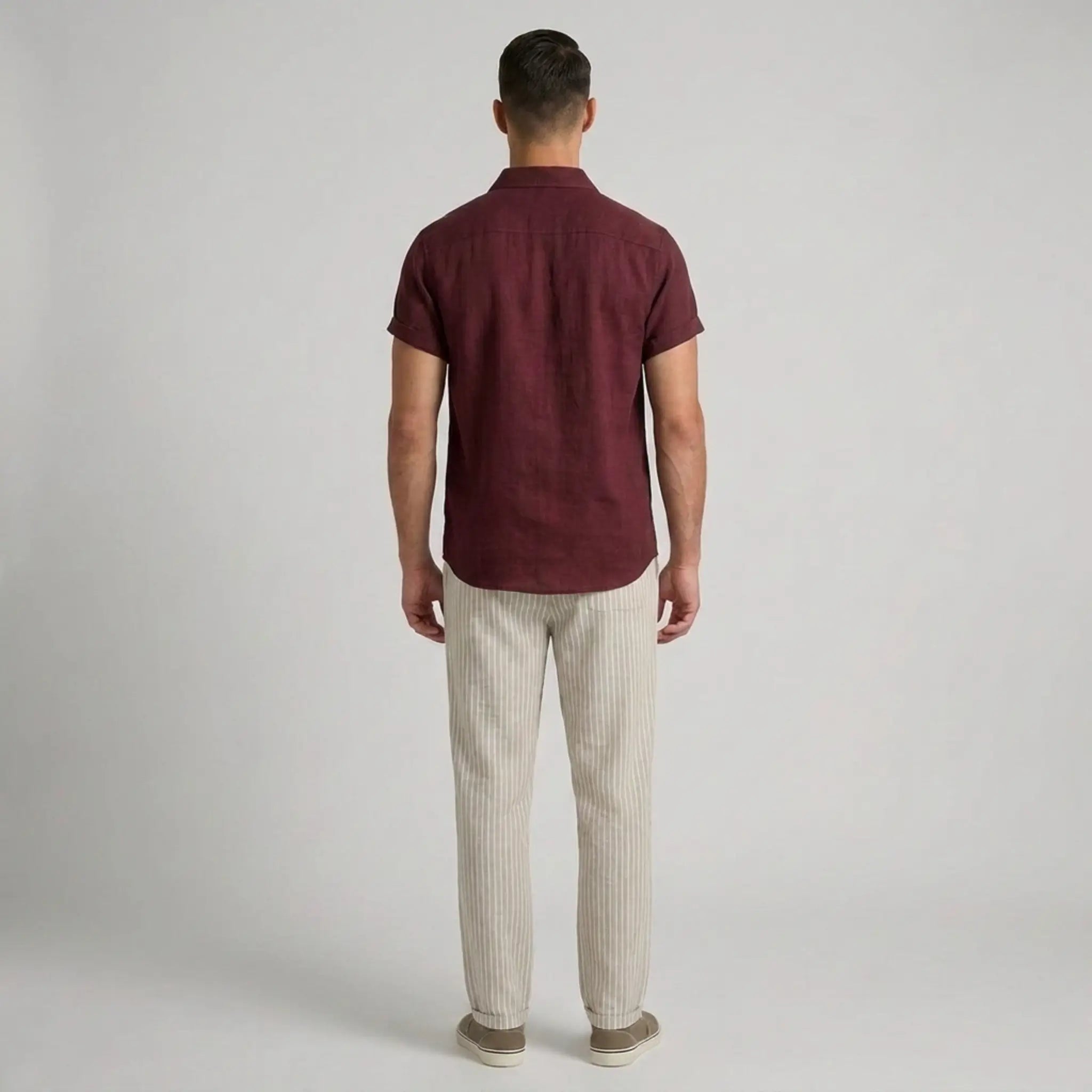 Man wearing a maroon polo shirt and beige striped pants on a gray background