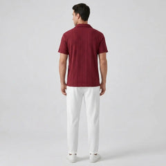 Man wearing a maroon polo shirt and white pants back view on a light gray background