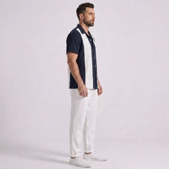 Man wearing a navy and white button-up shirt with white pants on a light gray background