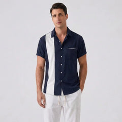 Man wearing a navy and white patterned shirt with white pants on a light gray background